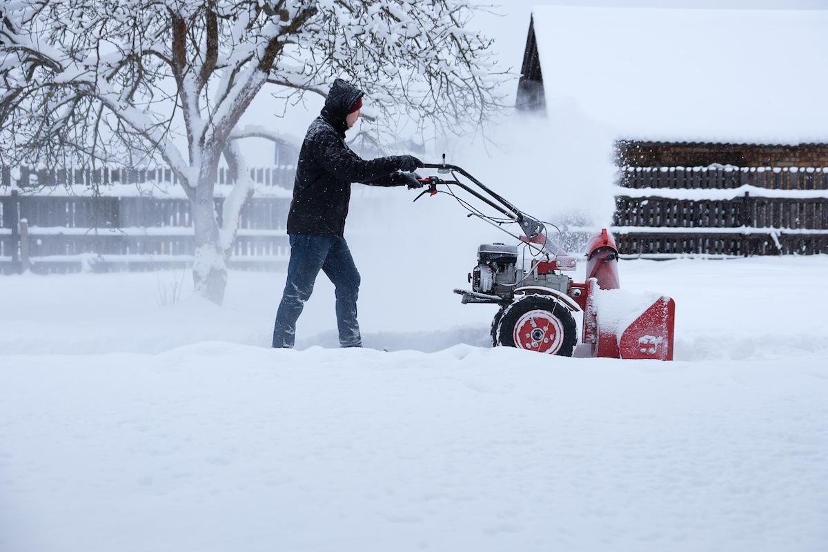 a young man clearing snow in his backyard with wheeled snow blower