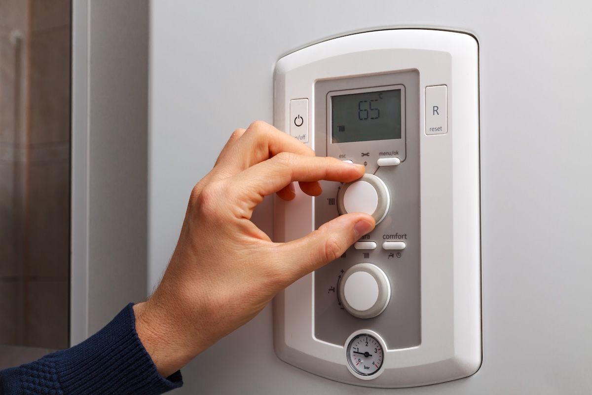 A hand turning a dial to regulate temperature on 65 degree in control panel of central air conditioning thermostat.