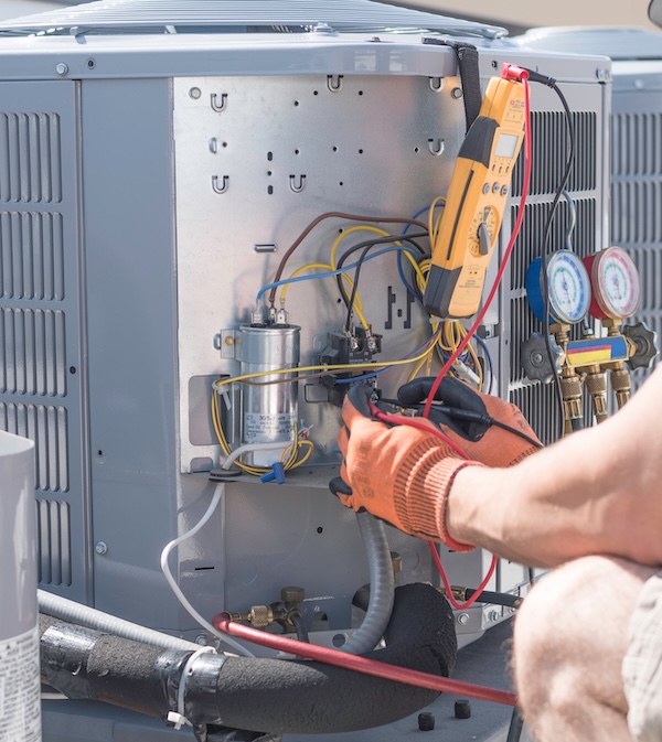 Hvac repair technician using a volt meter to test components on an air conditioner condenser.