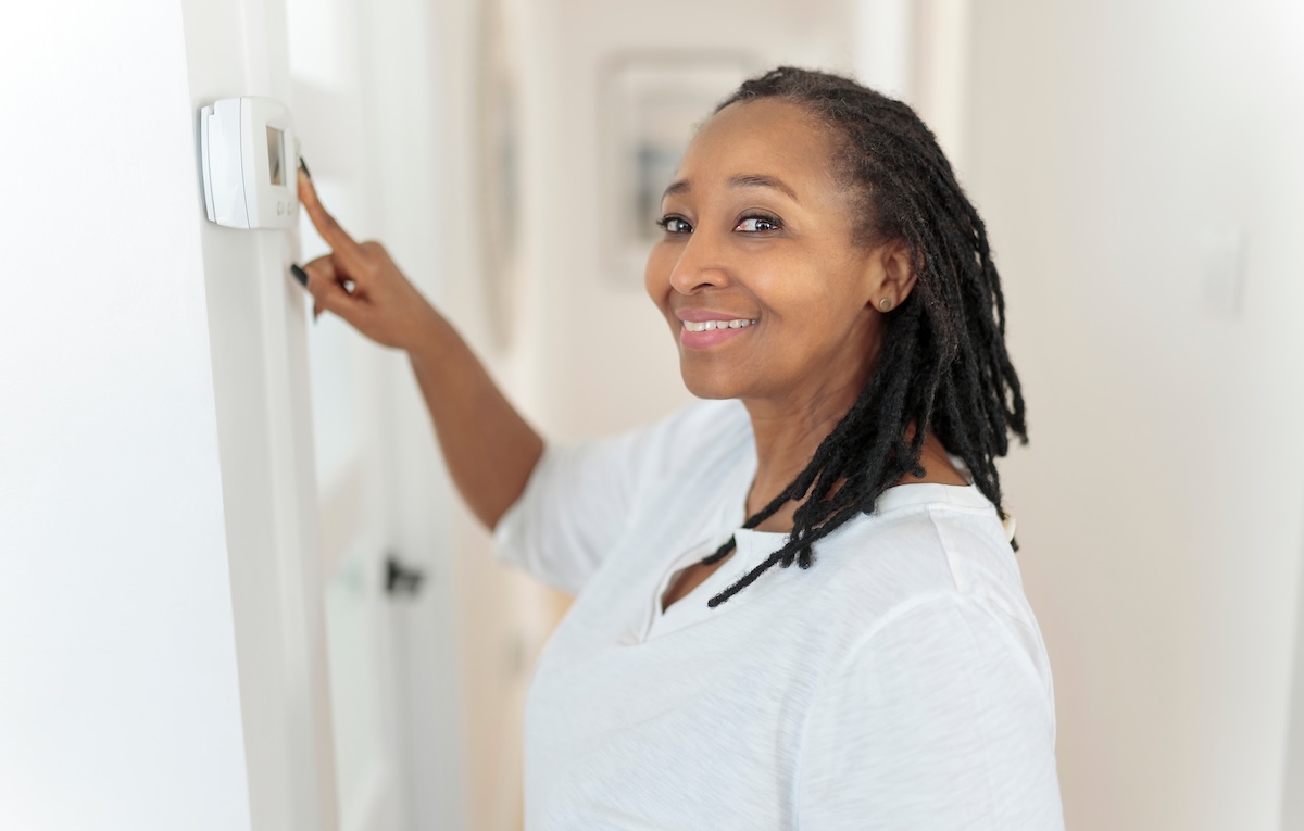 A woman adjusts the central air temperature using a wall panel.