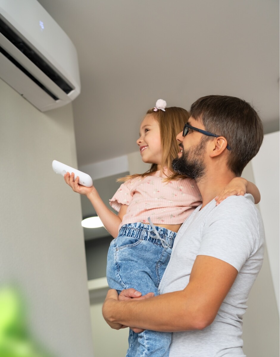 A father lifts up his little girl, who is holding a remote control for the ductless mini split air conditioning system in their home