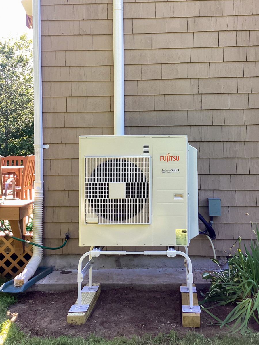 The outdoor component of a ductless mini split air conditioning system sits on elevated rails at the back of a residence in Worcester, MA.